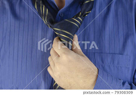 An adult man in a blue shirt is tying a tie An adult man in a blue shirt is tying a tie 79308309