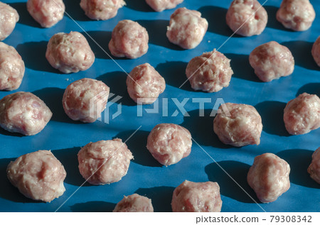 Raw shaped meatballs in sunbeams on blue. 79308342