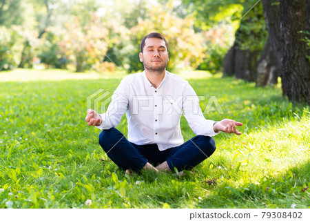 Young man meditates in lotus pose on green grass 79308402