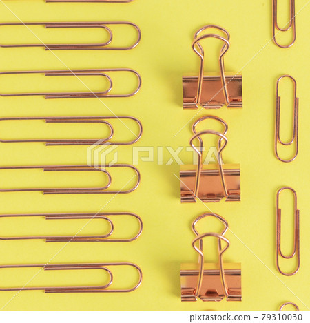 Copper stationery paper clips, clips, buttons are laid out in a certain rhythm on a yellow background. The concept of minimalism, business, success, wealth 79310030