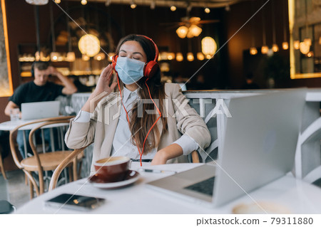 A girl sitting in a coffee shop with headphones. Coronavirus outbreak. A girl sitting in a coffee shop with headphones. Coronavirus outbreak. 79311880