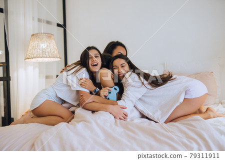 Positive young girls women friends indoors on bed at the hen party at home. 79311911