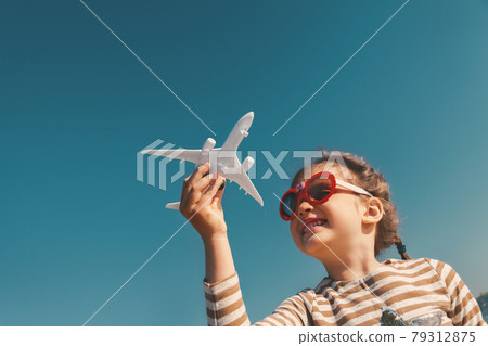 Little girl with toy plane in her hands against blue sky Little girl with toy plane in her hands against blue sky 79312875