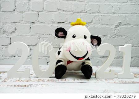 2021 Happy New Year and Cute Funny cow doll with space copy on white brick wall and wooden background 2021 Happy New Year and Cute Funny cow doll with space copy on white brick wall and wooden background 79320279