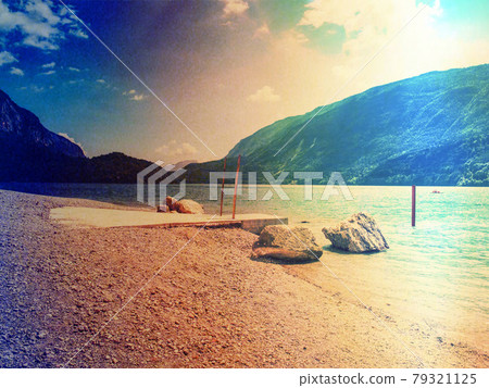 Jet pier and pebbles beach at bblue alpine lake. Warm sunrays over hills. Jet pier and pebbles beach at bblue alpine lake. Warm sunrays over hills. 79321125