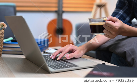 Close up view woman holding coffee cup and using laptop in living room. 79322389