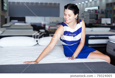 Female sitting on mattress for testing it 79324005