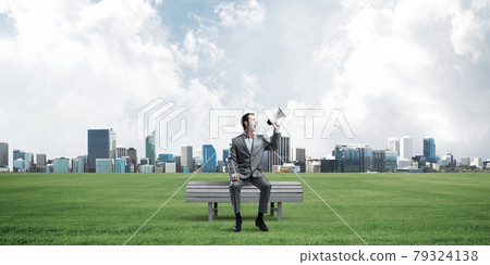 Businessman in summer park announcing something in loudspeaker and cityscape at background 79324138