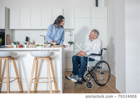 Young woman making breakfast, her handicapped husband sitting near 79324808