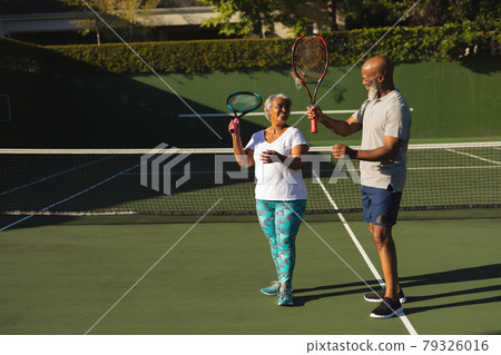 Portrait of smiling senior african american couple with tennis rackets on tennis court 79326016