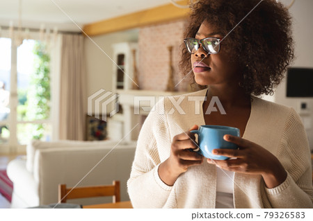 Thoughtful african american woman standing in dining room holding cup of coffee Thoughtful african american woman standing in dining room holding cup of coffee 79326583