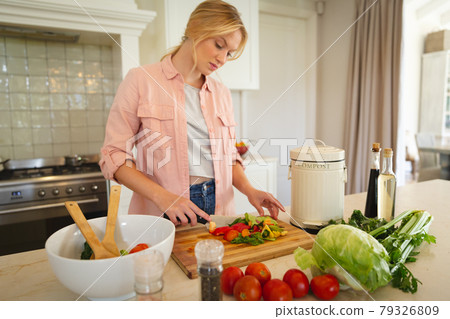 Caucasian woman standing in kitchen preparing food, chopping vegetables for salad Caucasian woman standing in kitchen preparing food, chopping vegetables for salad 79326809