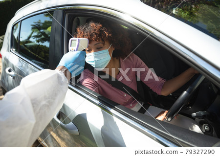 Medical worker wearing ppe suit taking temperature of african american woman sitting in car Medical worker wearing ppe suit taking temperature of african american woman sitting in car 79327290