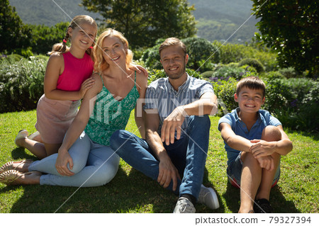 Portrait of happy caucasian couple with daughter and son outdoors, sitting in sunny garden Portrait of happy caucasian couple with daughter and son outdoors, sitting in sunny garden 79327394