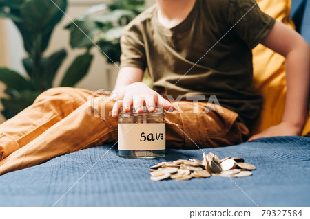 Close up of Little child kid boy hands grabbing and putting stack coins in to glass jar with save label. Donation, saving money, charity, family finance plan concept 79327584