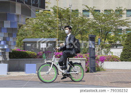 Asian young man with mask riding sharing bicycle on the way tro work Asian young man with mask riding sharing bicycle on the way tro work 79330232