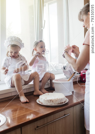 Children in the kitchen cook with their parents. Making homemade cake, pastries or cookies for the whole family. Happy childhood concept. Little twin sisters in kitchen aprons and chef hats Children in the kitchen cook with their parents. Making homemade cake, pastries or cookies for the whole family. Happy childhood concept. Little twin sisters in kitchen aprons and chef hats 79330595