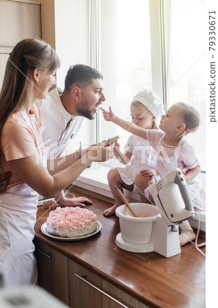 Children in the kitchen cook with their parents. Making homemade cake, pastries or cookies for the whole family. Happy childhood concept. Little twin sisters in kitchen aprons and chef hats 79330671