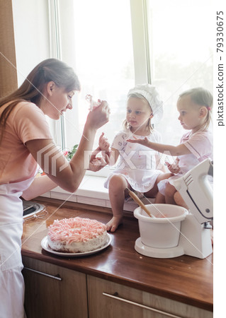 Children in the kitchen cook with their parents. Making homemade cake, pastries or cookies for the whole family. Happy childhood concept. Little twin sisters in kitchen aprons and chef hats Children in the kitchen cook with their parents. Making homemade cake, pastries or cookies for the whole family. Happy childhood concept. Little twin sisters in kitchen aprons and chef hats 79330675