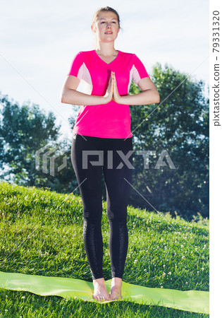 Smiling adult woman in pink T-shirt is staying and practising meditation Smiling adult woman in pink T-shirt is staying and practising meditation 79331320