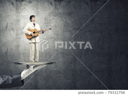 Businessman on metal tray playing acoustic guitar against concrete wall background 79332706