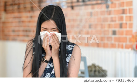 Sick lady blowing nose sneezing in paper tissue while sitting in her office. Sick lady blowing nose sneezing in paper tissue while sitting in her office. 79333460