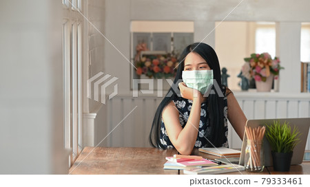 A young female wearing mask sitting in office while looking out the windows. A young female wearing mask sitting in office while looking out the windows. 79333461