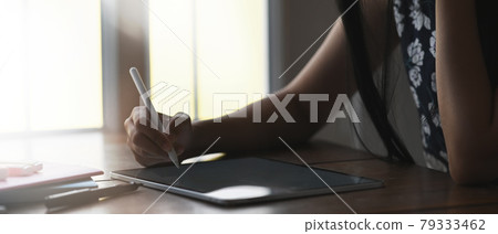 Cropped shot of female freelancer working on digital tablet while sitting next to window in office. Cropped shot of female freelancer working on digital tablet while sitting next to window in office. 79333462