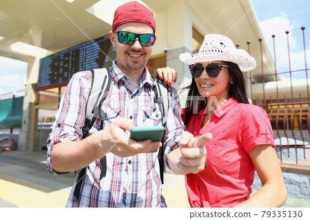 Young man and woman in sunglasses standing on platform of train and looking at screen of mobile phone Young man and woman in sunglasses standing on platform of train and looking at screen of mobile phone 79335130