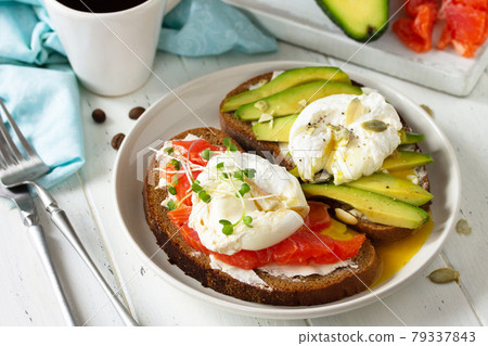 Morning breakfast. Poached egg boiled sandwich with avocado, salmon and coffee on a wooden table. Morning breakfast. Poached egg boiled sandwich with avocado, salmon and coffee on a wooden table. 79337843