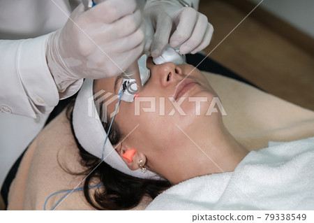 Close up of a woman getting laser face treatment procedure in medical salon center. Skin rejuvenation and beauty concept Close up of a woman getting laser face treatment procedure in medical salon center. Skin rejuvenation and beauty concept 79338549