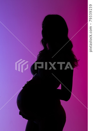 Beautiful young pregnant woman in lingerie is happily stroking her belly in studio in beautiful neon purple lighting. Concept of beauty and expectation of meeting with your beloved baby 79339159