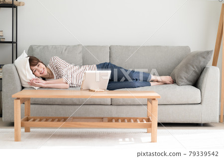 A woman looking at a tablet while lying on the sofa 79339542