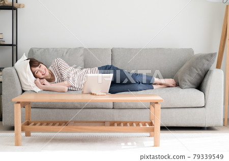 A woman looking at a tablet while lying on the sofa A woman looking at a tablet while lying on the sofa 79339549