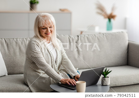 Mature woman sitting on couch and working on computer Mature woman sitting on couch and working on computer 79342511
