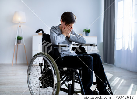 Depression in disabled teenagers. Unhappy handicapped teen boy in wheelchair crying at home Depression in disabled teenagers. Unhappy handicapped teen boy in wheelchair crying at home 79342618