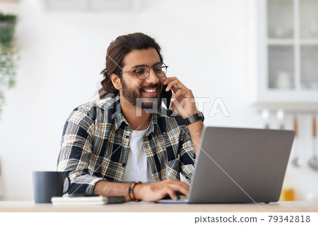 Smiling arab man freelancer talking on phone and taking notes 79342818