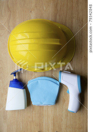 Top view of sanitizer bottle , thermometer gun blue mask and yellow hard hat on wooden background	 79342848