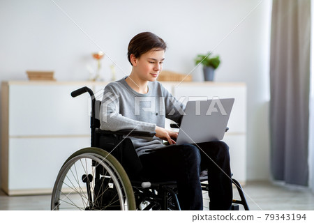 Home schooling concept. Smart disabled teenager in wheelchair using laptop for online education or communication at home Home schooling concept. Smart disabled teenager in wheelchair using laptop for online education or communication at home 79343194