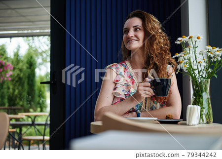 Attractive woman with curly hair drinking coffee sitting at the table in cozy coffee house Attractive woman with curly hair drinking coffee sitting at the table in cozy coffee house 79344242