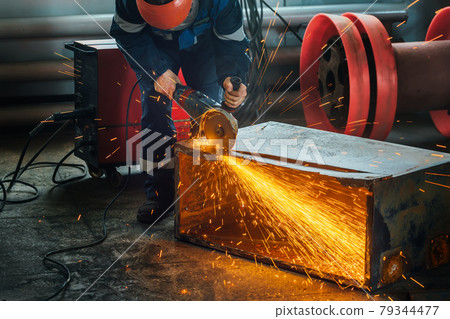A worker cuts metal with a hand grinder in the production shop and bright sparks fly. A genuine 79344477