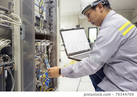 Network administrator holding laptop in hand working Configuration with core switch on rack cabinet in data center 79344709