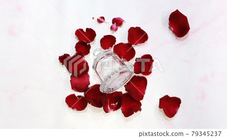 An empty bell-shaped glass jar with the lid on, laying on the surface, with red rose petals spreading around. An empty bell-shaped glass jar with the lid on, laying on the surface, with red rose petals spreading around. 79345237