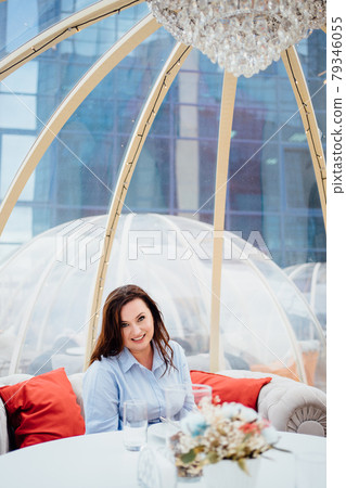 woman in a blue dress sits at tables in a cafe in the shape of a igloo on roof.  79346055