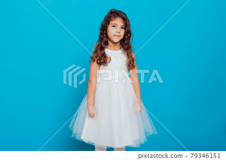 Beautiful little curly girl 5 years old in a white dress on a blue background Beautiful little curly girl 5 years old in a white dress on a blue background 79346151