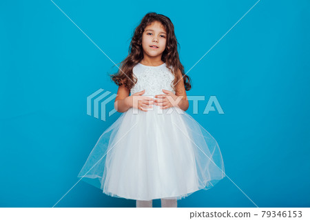 Beautiful little curly girl 5 years old in a white dress on a blue background Beautiful little curly girl 5 years old in a white dress on a blue background 79346153