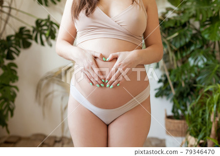 Pregnant woman making heart on her belly in sport swimsuit close up 79346470