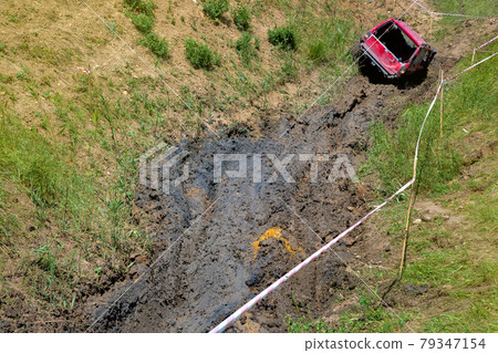 An open pit with slopes and off-road terrain for competition driving through the swamp on off-road vehicles with increased cross-country ability, dirty red car on mud landscape. An open pit with slopes and off-road terrain for competition driving through the swamp on off-road vehicles with increased cross-country ability, dirty red car on mud landscape. 79347154