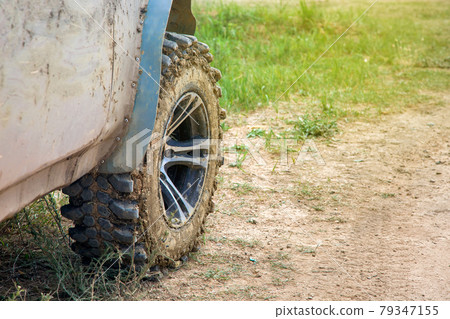 wheel with disc dirty in a swamp off-road tire treads on a rough dusty road with grass close-up. 79347155