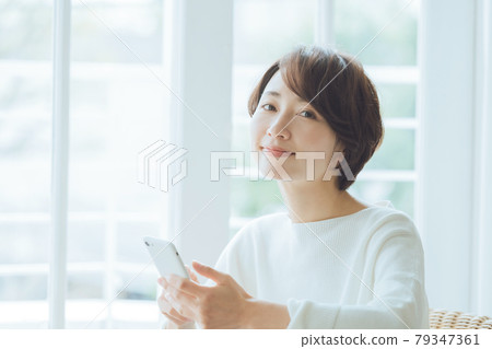 Middle-aged woman operating a smartphone in the room Middle-aged woman operating a smartphone in the room 79347361